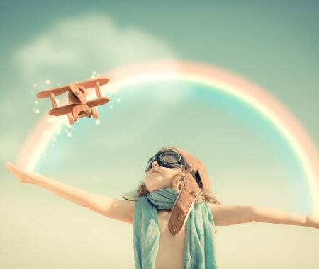 Happy kid playing with toy airplane against summer sky background